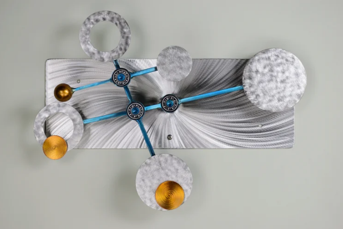 Large brushed-steel kinetic sculpture with teal spokes and gold accents